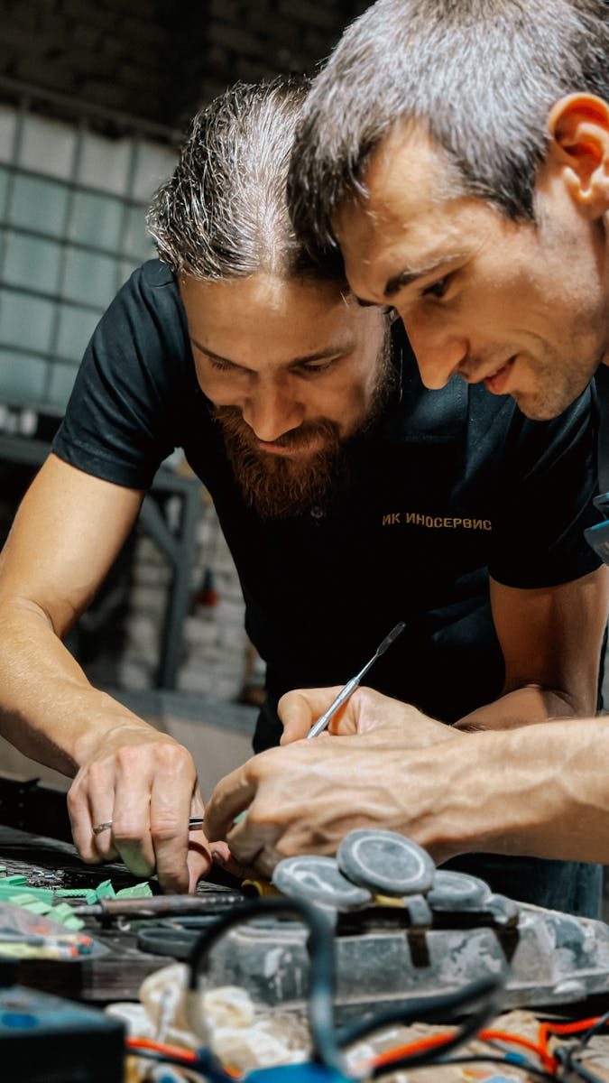 Two adults collaborating on detailed crafting work indoors, focusing closely.