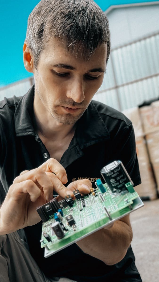 Focused technician inspecting electronic circuit board outdoors, concept of technology and repair.