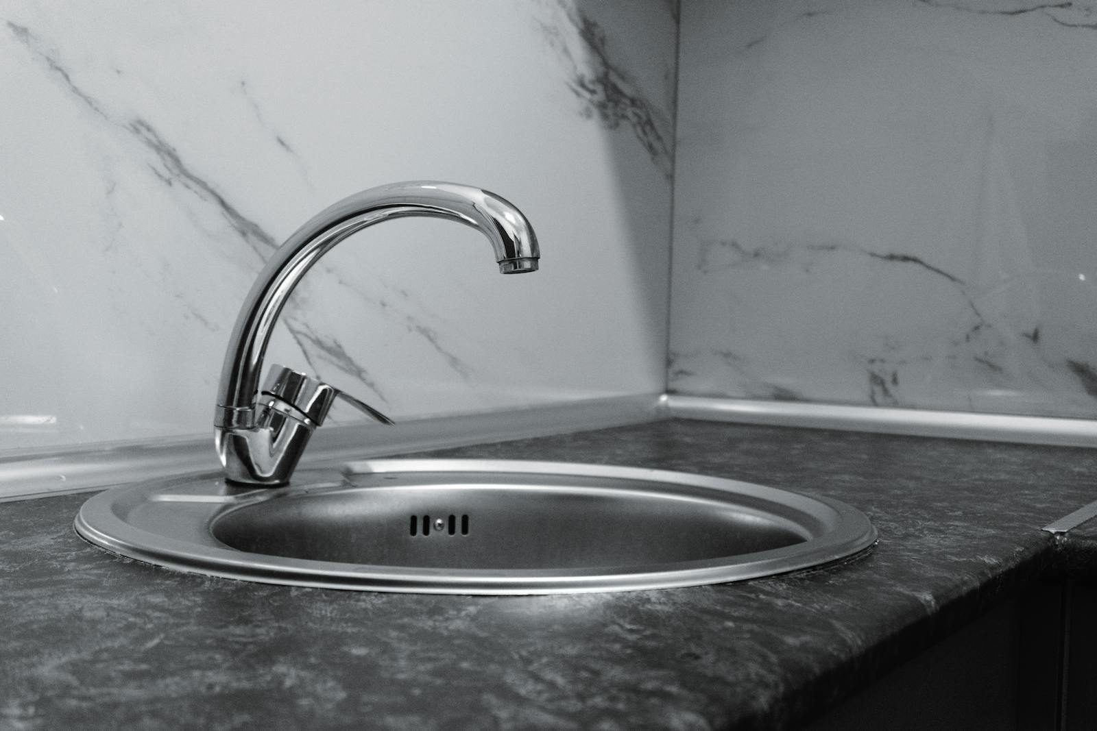 Stainless steel kitchen sink and faucet against marble backsplash in a modern kitchen.